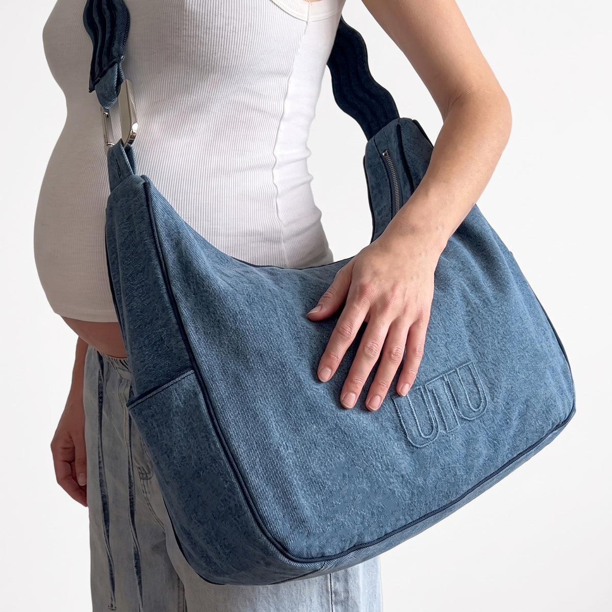 A pregnant mom holding her toddler, the denim MAMEI Bag on her shoulder